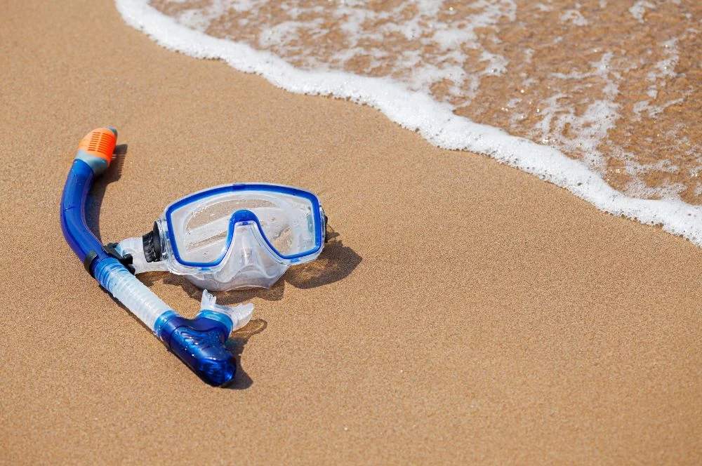 A snorkel mask and snorkel on the sand at the water's edge