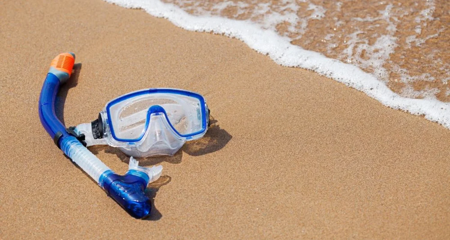 A snorkel mask and snorkel on the sand at the water's edge